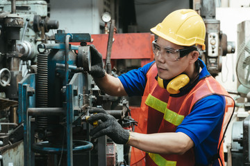 A mechanical engineer or worker with yellow safety helmet and goggles at work on production in a...