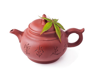 Chinese clay teapot with green japanese maple leaf isolated on a white background. Chinese inscription on teapot - "Be satisfied with real life"