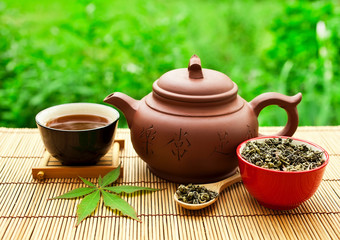 Chinese tea ceremony in the garden with dry green tea in spoon on a bamboo table.
