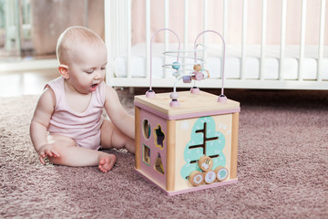 Cute baby girl playing with wooden activity toy.