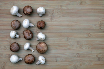 Fototapeta na wymiar White and brown crimini mushrooms arranged in an alternating pattern on the left side of a bamboo board