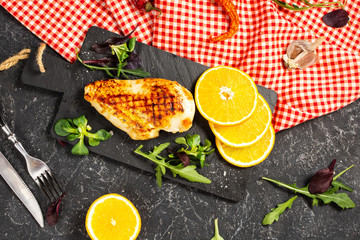 Grilled chicken fillets with orange on slate plate. Black stone background.