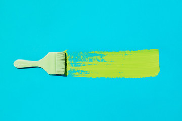 Flatlay of colored brush with swoosh of green paint on blue