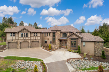 Exterior of beautiful and large new luxury home with blue sky and clouds. Features three car garage and blend of old world and traditional design