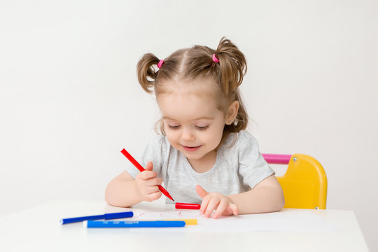 child a girl two years old sits at a table and draws on a white background
