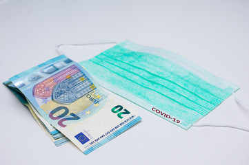 20 euro banknotes next to a medical face mask. The word COVID-19 is written in red on the mask