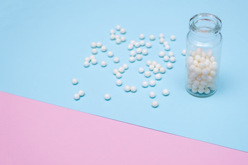 Homeopathic globules in a glass bottle and scatterred near on double colored pink and blue background, naturopathy concept, copy space