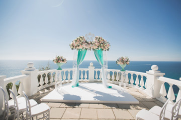 Elegant wedding arch with fresh flowers, vases on the background of the ocean and blue sky.