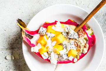 Mango smoothie with granola and coconut chips in dragon fruit, top view. Healthy vegan breakfast concept.