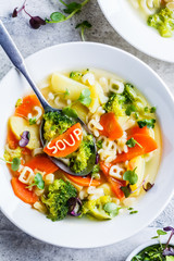 Healthy kids alphabet soup with broccoli, carrot and potato in white plates, top view.