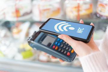 A woman's hands close up is holding a payment terminal and paying for a purchase using a smartphone. On the phone screen, the wi-fi network. The concept of NFC, business and banking transactions