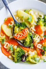 Healthy kids alphabet soup with broccoli, carrot and potato in white plate, top view.