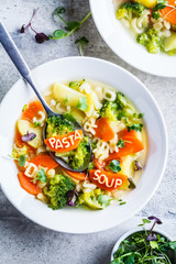 Healthy kids alphabet soup with broccoli, carrot and potato in white plates, top view.