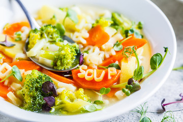 Healthy kids alphabet soup with broccoli, carrot and potato in white plate.