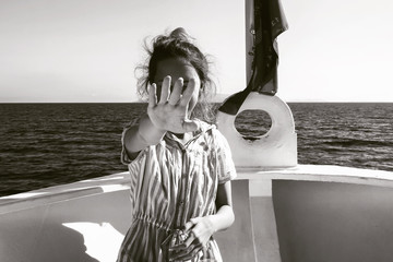 Black and white photograph of a girl on a yacht. She extended her palm forward to cover her face.