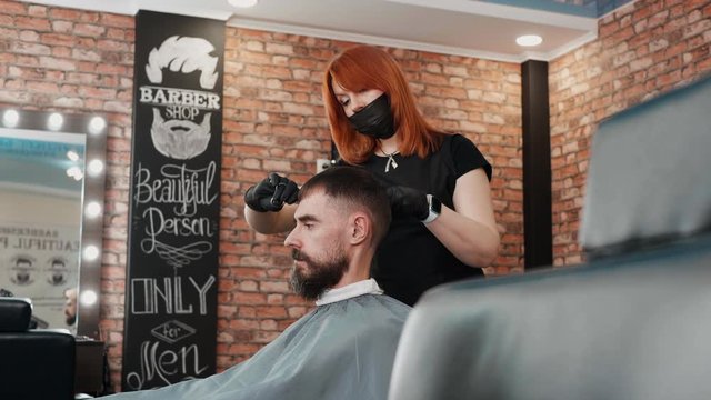 Hairdresser cutting and combing hair of client. Professional female hairstylist in facial mask working with man at workplace. Haircut concept