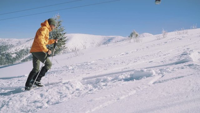  High mountaineer dressed bright orange softshell jacket using a trekking poles ascending the snowy mountain summit. Active people 4K concept footage