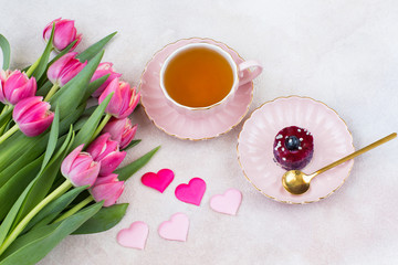 Fototapeta na wymiar a bouquet of pink tulips, a cup of tea, cake and satin hearts