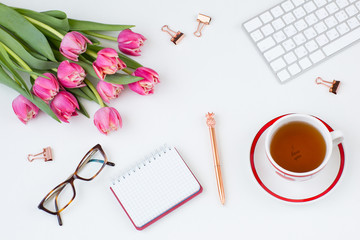 keyboard, paper clips, glasses, notebook, pen, tea cup and bouquet of pink tulips