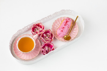 on the table is a cup of tea, cake and three buds of tulips 