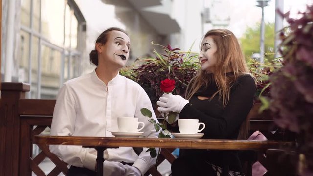Two happy mime on a date in the cafe. Happy man giving a flower to his girlfriend. Romantic date