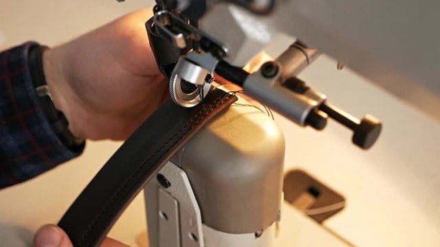 Sewing machine needle in motion. A close-up of the needle of a sewing machine moves quickly up and down. The tailor sews a leather belt at a sewing workshop. Leather sewing process