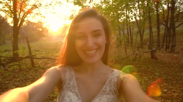 Point of view shot of attractive bride is posing into camera against sunny rays at sunset with tender smile. Slow motion