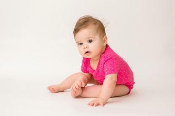 healthy baby girl in a pink bodysuit sits on a white background. space for text