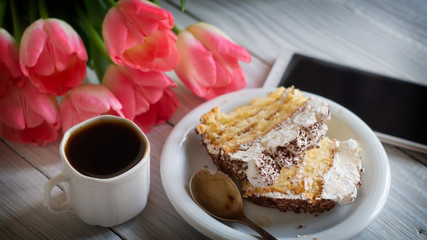 Tiramisu cake, pink tulips and cup of coffee on a white wooden table