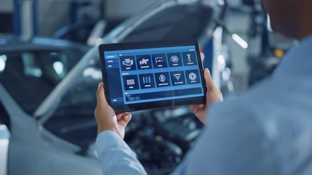 Car Service Manager or Mechanic Uses a Tablet Computer with a Futuristic Interactive Diagnostics Software. Specialist Inspecting the Vehicle in Order to Find Broken Components In the Engine Bay.