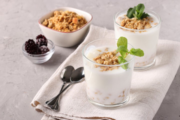 Two servings of homemade natural yogurt with granola and mint in glasses on a gray background, Diet and weight loss control concept, Copy space