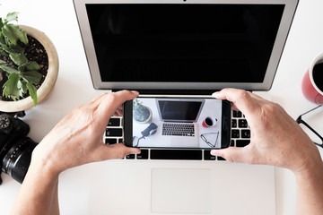 Human hands of a senior woman over the laptop keyboard doing a photograph of the desk - camera and coffee cup on the table
