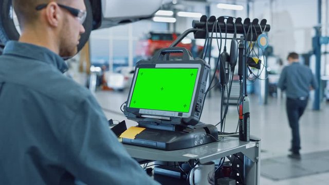 Car Service Mechanic is Running a Diagnostics Software on an Advanced Computer with Green Screen. Specialist Inspecting the Vehicle in Order to Find Broken Components and Errors in Data Logs.