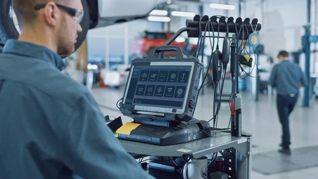 Car Service Manager or Mechanic is Running an Interactive Diagnostics Software on an Advanced Computer. Specialist Inspecting the Vehicle in Order to Find Broken Components and Errors in Data Logs.