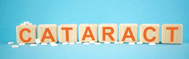 Cataract - word made on wooden cubes on light blue backround with tablets (pills) around. Healthy...