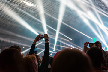 A crowd of people at the concert have fun and dance to the music at the concert. Gray background and beams. Rear view. The concept of entertainment and relaxation