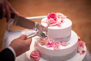 Wedding tradition in Poland. Bride and groom make the first cut of their wedding cake. Wedding reception celebration background. Sweet dessert for a couple.