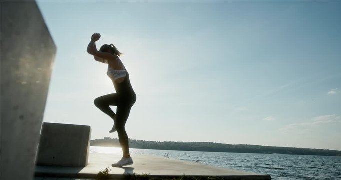 Sportswoman jumping on cube on embankment
