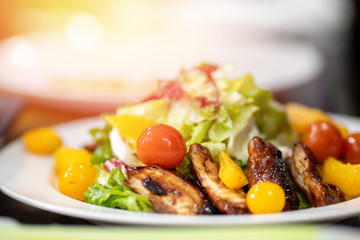 Juicy healthy salad with fried chicken, tomatoes, herbs, oranges, almonds on white plate