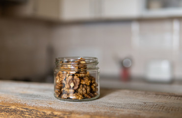 Walnut in a jar which standing on a white vintage table with a kitchen on background. Walnuts is a healthy vegetarian protein nutritious food. Walnut on rustic old wood.