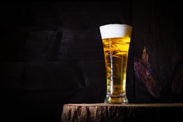 light, foamy, tasty beer in a glass on a black wooden background, stands on a wooden saw, hemp.