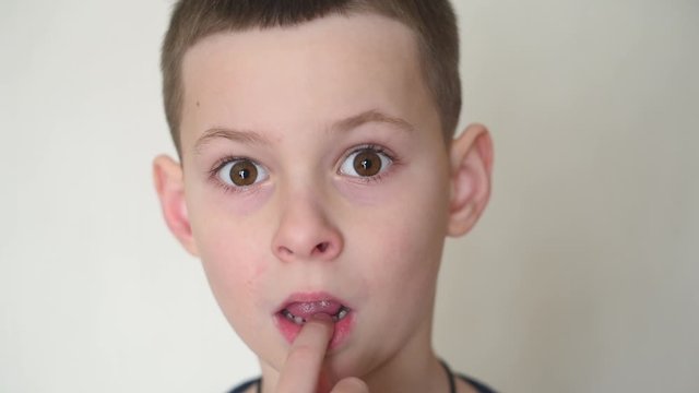 a small child boy loosens a baby tooth with his finger .