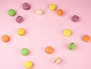many multi-colored round baked macarons cakes on a light pink background