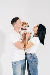 Young man and her boyfriend with their dog at studio. Young owners kissing pet. young and beautiful couple holding dog in arms with love and playing with him, against a white background