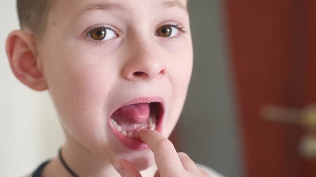a small child boy loosens a baby tooth with his finger .