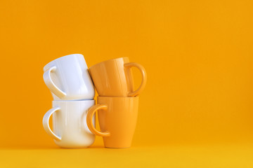 White and yellow coffee cups stack on yellow background
