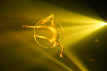 Flexible young woman make performance on aerial hoop, flexible back on aerial hoop, aerial circus show, yellow light. Flexible woman gymnast upside down on hoop. Show in night club