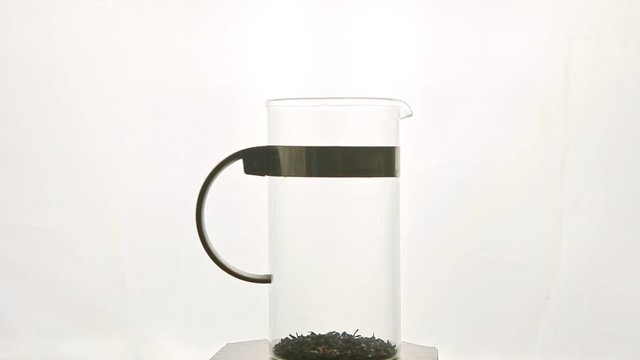 tall glass teapot with tea leaves spinning around on pedestal against white