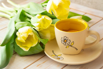 Yellow tulips bouquet and a cup of tea with lemon on white shabby background