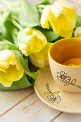 yellow tulips, pastel yellow cup of tea with lemon on a white shabby wooden background. Vertical image